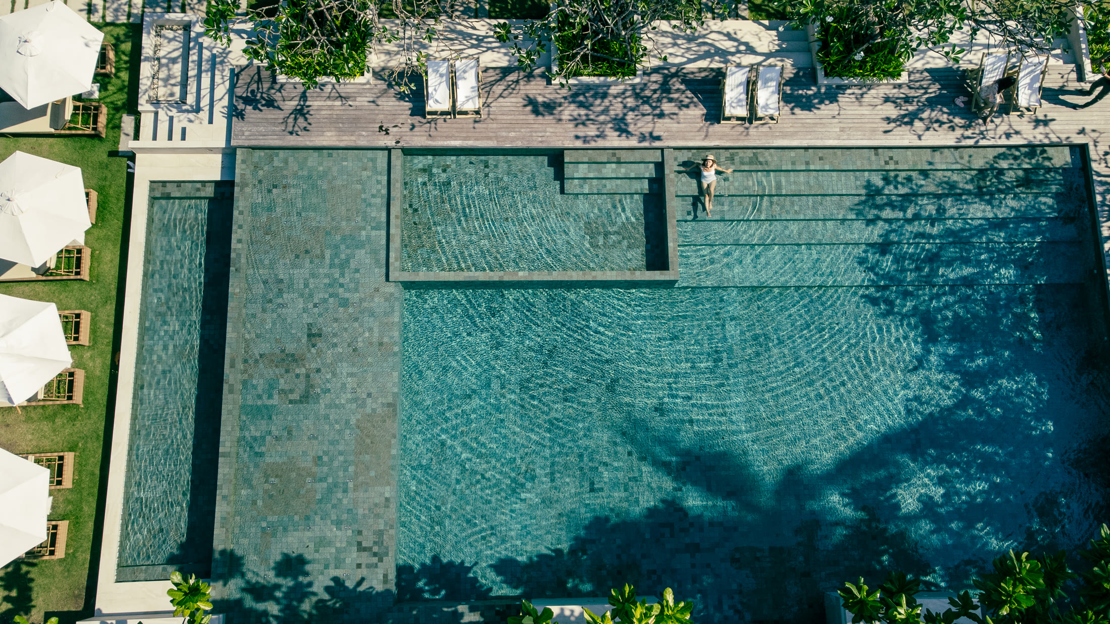 ภาพโดรนมุมตรงลงสระว่ายน้ำรีสอร์ตและเงาต้นมะพร้าว