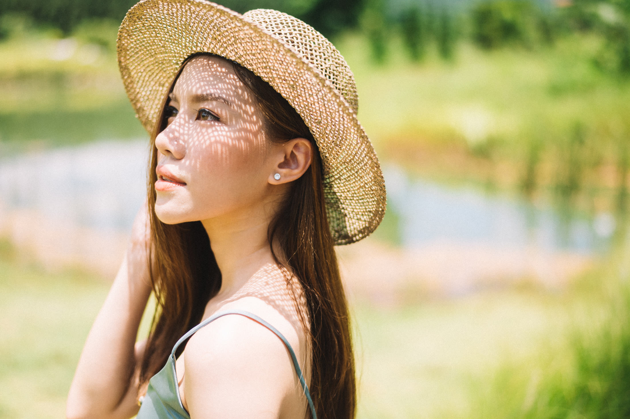 หญิงสาวสวมหมวกสานมองขึ้นท้องฟ้า แสงลอดปีกหมวก